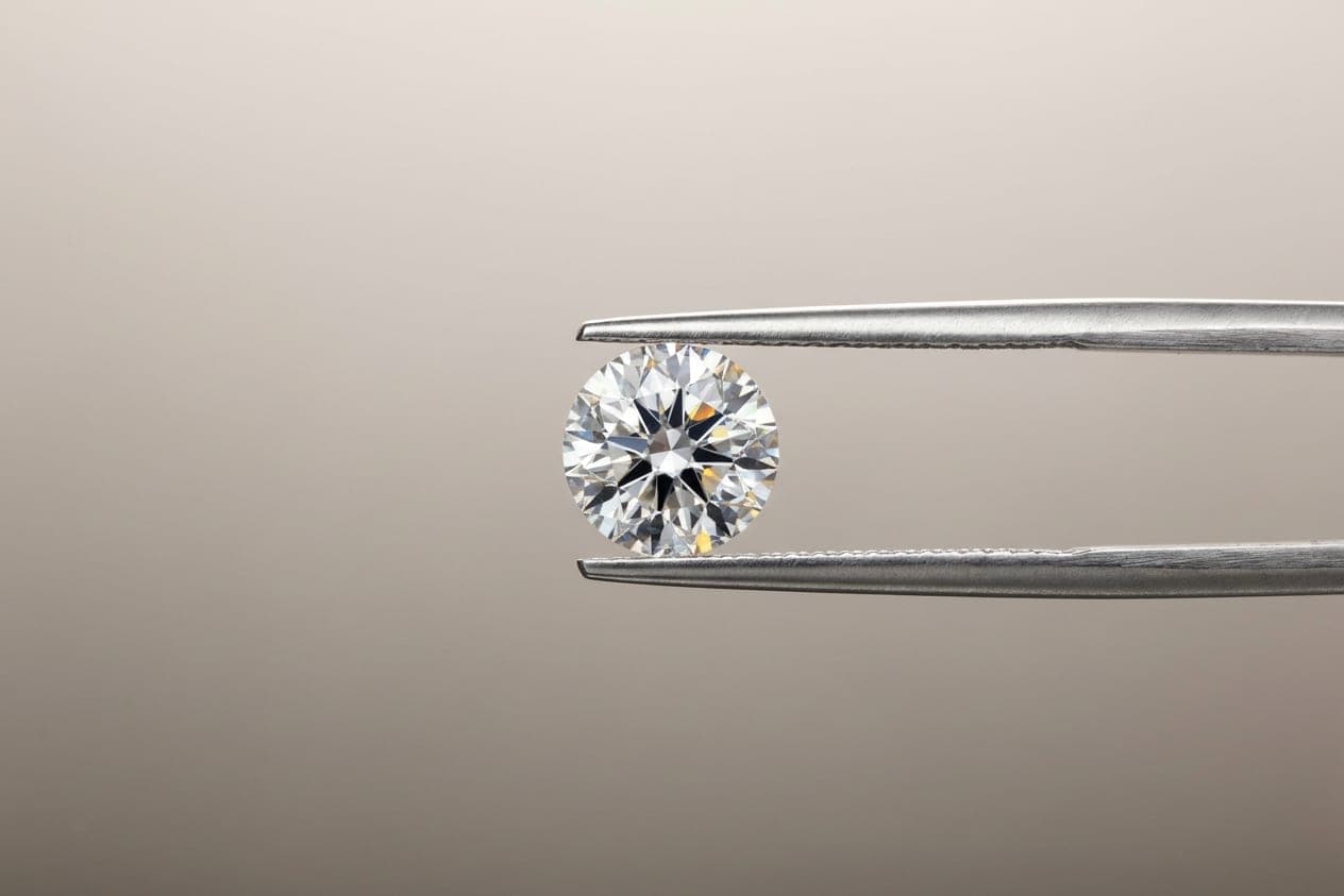 A loose brilliant-cut diamond held in tweezers against a grey background